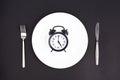 Time to eat. Lunch time. View from above on white plate with alarm clock and knife and pork near on black background. 5 p.m Royalty Free Stock Photo