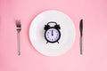 Time to eat. Lunch time. View from above on white plate with alarm clock and knife and pork near on pink background. 12 a.m Royalty Free Stock Photo