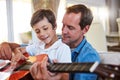 Time to get musical. Shot of a father and his young son sitting together in the living room at home playing guitar. Royalty Free Stock Photo