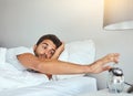 Time to get up. a tired young man sleeping in his bed while turning off the alarm clock. Royalty Free Stock Photo