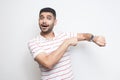 Time to go. Portrait of amazed funny bearded young man in striped t-shirt standing, pointing at his smart watch, looking at camera Royalty Free Stock Photo