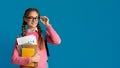 Time to learn. Confident smiling girl adjusts her glasses and holds notebooks and charts