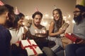 Young birthday man makes a wish and blows out the candles on the cake surrounded by his friends. Royalty Free Stock Photo