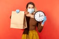 Time to order food, safe shopping on quarantine. Woman in protective mask holding paper bag and big clock Royalty Free Stock Photo