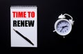 TIME TO RENEW is written in a white notepad near a white alarm clock on a black background Royalty Free Stock Photo