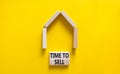 Time to sell house symbol. Concept words `Time to sell` on wooden blocks near miniature house. Beautiful yellow background, copy