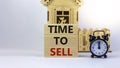 Time to sell real estate. Wooden blocks form the words `time to sell` near miniature house. Black alarm clock. Beautiful white