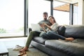 Time to splurge. Full length shot of an affectionate young couple using a laptop while relaxing on their sofa at home.