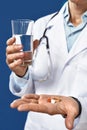 Time to take pills. Cropped shot of a male doctor in medical uniform holding pills and glass of water in front on camera Royalty Free Stock Photo