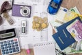 Passport, money, camera, watch, calculator, glasses, calendar toy car on wooden table.