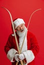 Cropped portrait of joyful senior man wearing Santa Claus costume, holding skis isolated over red background. Winter Royalty Free Stock Photo