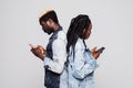 Time to use phones. Side portrait of african couple standing back to back holding mobile phones against white background Royalty Free Stock Photo