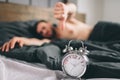 Time to wake up. Tired man in the bed not happy. Mature guy holding alarm clock while checking time for work Royalty Free Stock Photo