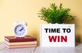 TIME TO WIN written in a white notebook near a white alarm clock on a yellow table. Motivational concept Royalty Free Stock Photo