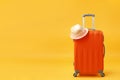 Time for travel, trip, adventure - an orange suitcase and a straw hat on a yellow background. Copy space Royalty Free Stock Photo