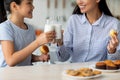 Time for vitamins. Asian girl and her young mother drinking milk in kitchen, enjoying calcium drink, closeup, crop