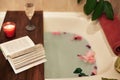 Bath with flower petals. Book, candles and glass of wine on a wood tray. Organic Spa Relaxation in comfort cozy bathroom Royalty Free Stock Photo
