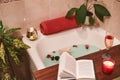 Bath with flower petals. Book, candles and glass of wine on a wood tray. Organic Spa Relaxation in comfort cozy bathroom Royalty Free Stock Photo