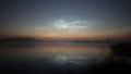 Timelapse silvery mesospheric clouds above the lake float and are reflected in the water