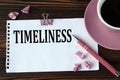 TIMELINESS - word on a white sheet on a wooden brown background with a cup of coffee and a pen