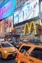 Times Square show billboards with people, yellow taxi traffic at night in New York