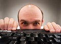 Timid nerd hiding under computer keyboard Royalty Free Stock Photo