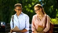 Timid students in glasses trying to make acquaintance, sitting on bench in park