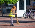Municipal female worker sweeping the pavement with broomstick, in the center of Timisoara