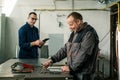 A tinsmith is measuring in his workshop with a colleague engineer who is taking notes on tablet Royalty Free Stock Photo