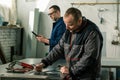 A tinsmith is measuring in his workshop with a colleague engineer who is taking notes on tablet Royalty Free Stock Photo