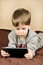 Tinted image little boy lying on the bed and plays on the tablet