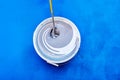 Stirring rod mixing and tinting paint for walls, house painter tinted paint in bucket on blue background. Royalty Free Stock Photo