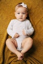 Tiny baby girl with a flower on her head in a white bodysuit lies on a yellow blanket with her hands on her tummy Royalty Free Stock Photo