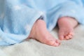 Tiny bare legs and feet of newborn covered with a blue soft warm blanket. Little baby sleeps on white blanket on bed. Dermatology