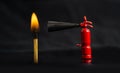 Tiny fire extinguisher close to a burning match against a lit black background, macro shot Royalty Free Stock Photo