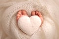 The tiny foot of a newborn baby. Soft feet of a new born in a white wool blanket Knitted white heart in the legs of baby Royalty Free Stock Photo