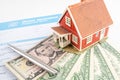 Tiny house together with home insurance form and dollar currency bills laying on white office table. Royalty Free Stock Photo