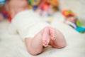 Tiny legs of a baby in a white bodysuit. An admiring innocent girl lying in a comfortable crib in the bedroom. Royalty Free Stock Photo