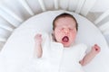 Tiny new born baby screaming loud in a white round crib