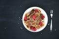 Tiny pancake cereal - trendy quarantine food. Mini pancakes in bowl with fresh raspberries and coconut flakes on black background Royalty Free Stock Photo