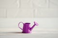 Tiny purple watering can, standing on white wooden background with brick wall, with copyspace Royalty Free Stock Photo