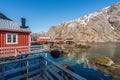 Tiny red rorbuer cabins in Nusfjord, Lofoten in Norway during sunny and calm weather with the fjord and the mountains next to it.