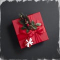 A tiny shiny red box stands on a large gift box decorated with a spruce branch against a black, not fully painted