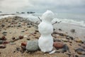 tiny snowman with branches hands raised up stands on a sandy beach among the pebbles and looks at the waves Royalty Free Stock Photo