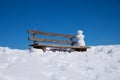 Wooden bench with tiny snowman, blue sky