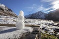 A tiny snowman stands against the backdrop of snow-capped mountains on a sunny day. Beautiful autumn valley in the background