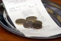 A tip of coins on a plate with a receipt in a restaurant