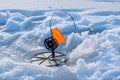 Tip-up fishing rod with orange signal flag in backlight ready for pike bite in a frozen river hole, footprints in snow