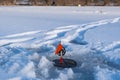 Tip-up fishing rod with orange signal flag ready for pike bite in a frozen river hole, human footprints in wet snow