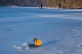 Tip-up fishing rod with orange signal flag in sunlight, ready for pike bite in a frozen river hole, fisherman figure